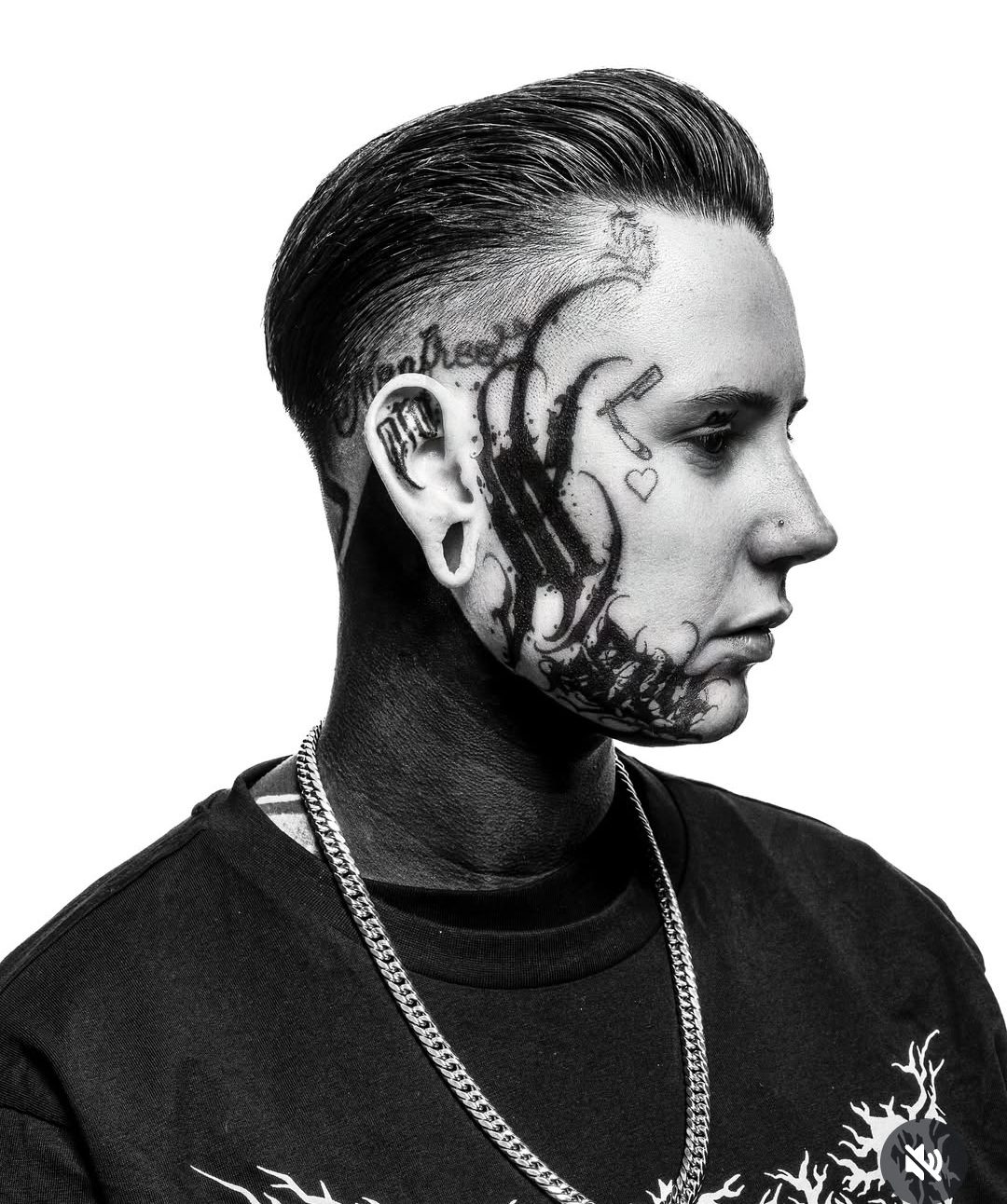 Zijaanzicht in zwart-wit van een barbier met tatoeages en strak naar achteren gekamd haar