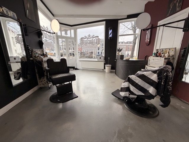 Het interieur van de shop: twee barbierstoelen met gestreepte capes voor de grote ramen